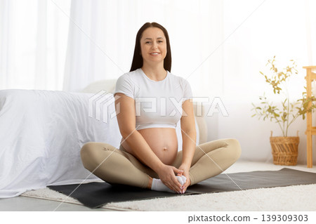 Peaceful pregnant woman sitting in lotus pose on yoga mat at home 139309303
