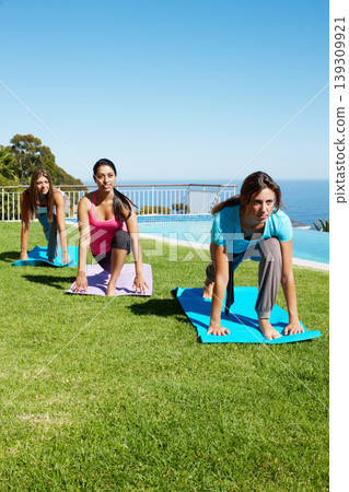 Ocean, yoga and group of women on grass together for fitness, exercise or mindfulness resort. Nature, pilates and happy friends at outdoor holistic health retreat for wellness, balance and sunshine. 139309921