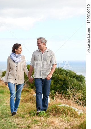 Old couple, walking and holding hands in nature on holiday, vacation or support in retirement. Love, man and woman with conversation, care or happiness in marriage together on grass at beach or park Old couple, walking and holding hands in nature on holiday, vacation or support in retirement. Love, man and woman with conversation, care or happiness in marriage together on grass at beach or park 139310050
