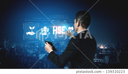 A business professional engages with a digital display of health, safety, and environmental icons, reflecting modern industry trends in an urban night setting. Sigmoid A business professional engages with a digital display of health, safety, and environmental icons, reflecting modern industry trends in an urban night setting. Sigmoid 139310223