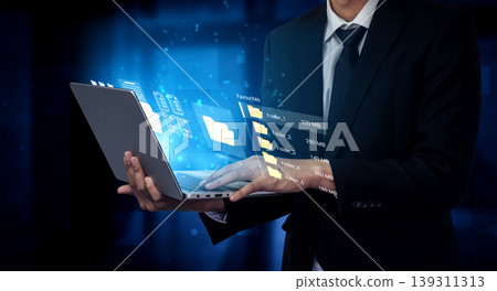Businessman using laptop with holographic interface displaying data files and analytics in a digital landscape, representing technology and innovation Ledger Businessman using laptop with holographic interface displaying data files and analytics in a digital landscape, representing technology and innovation Ledger 139311313