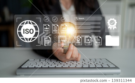 Business Person Holding Light Bulb with ISO Icons and Digital Interface Representing Quality Management and Certification in Modern Office Setting Gantry 139311344