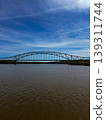 Steel Arch Bridge Spanning Calm River Under Blue Sky Scenic Waterfront Landscape Reflection Travel Infrastructure Landmark 139311744