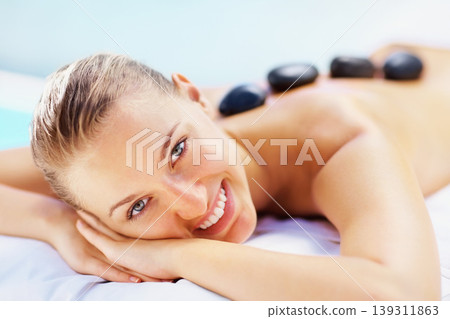 Portrait, spa bed and happy woman with hot stone back massage, relax or stress relief body treatment at wellness resort. Luxury, zen and face of female person at salon for healing, therapy or pamper Portrait, spa bed and happy woman with hot stone back massage, relax or stress relief body treatment at wellness resort. Luxury, zen and face of female person at salon for healing, therapy or pamper 139311863