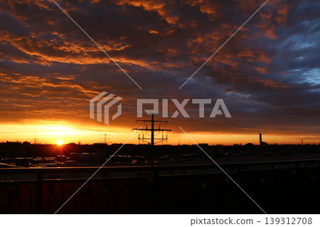 Dramatic Sunset Over Industrial Skyline with Silhouetted Pylon 139312708
