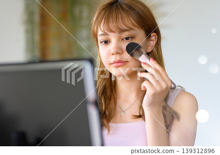 A woman puts on makeup while looking in the mirror. 139312896