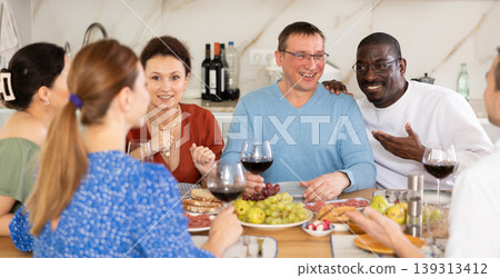 Cheerful adult friends dining and chatting in home kitchen Cheerful adult friends dining and chatting in home kitchen 139313412