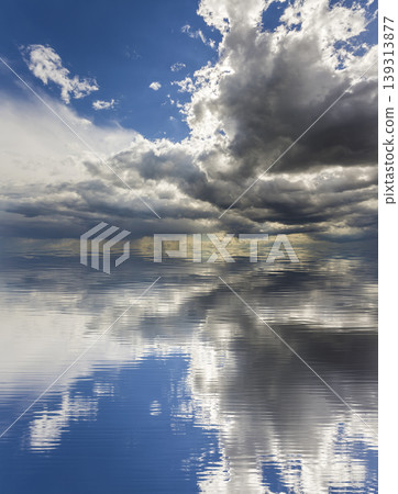 Fantastic view of bright white and dark puffy clouds lit by sun against deep blue sky reflecting in water. Beauty and power of nature, environment problems, ecology and climate changing concept. 139313877
