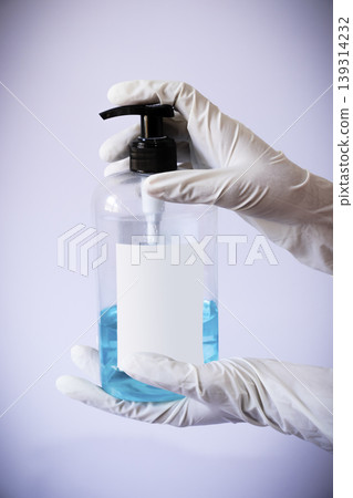 Presenting sanitizer bottle by both hands with medical latex gloves 139314232