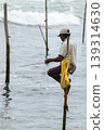 Stilt fisherman with his wooden rod facing side to the camera with his yellow pocket on the pole, fishing in a traditional unique method in Sri Lankan culture, sunny bright evening on the beach. 139314630