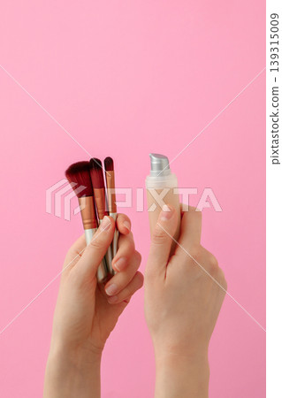 Hands show brushes and foundation on pink background Hands show brushes and foundation on pink background 139315009