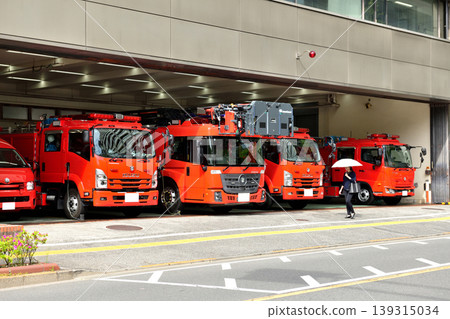 A woman walking in front of a fire station with a parasol. A woman walking in front of a fire station with a parasol. 139315034