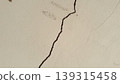 Close-up of a deep, irregular crack running through an aged, textured white concrete wall with minor surface damage. 139315458