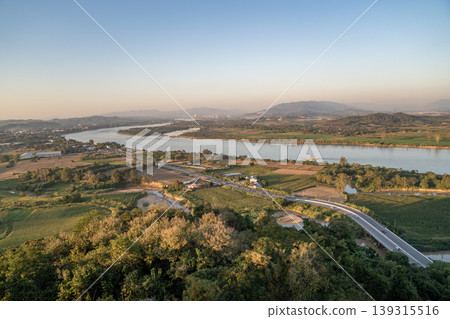 The Mekong River curves through farmland in Chiang Saen under soft light, with a winding road shaping a calm rural landscape pattern captured in 13 January 2023. The Mekong River curves through farmland in Chiang Saen under soft light, with a winding road shaping a calm rural landscape pattern captured in 13 January 2023. 139315516