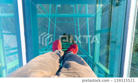 The shot of photographer feet with the reflection while walking on the transparent glass skywalk at Wat Phra That Pha Nago, Chiang Rai. The shot of photographer feet with the reflection while walking on the transparent glass skywalk at Wat Phra That Pha Nago, Chiang Rai. 139315521