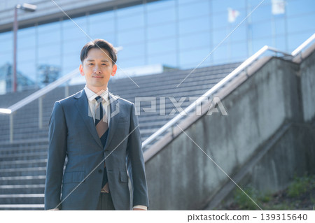 A business image of success and growth, featuring a sharp-looking salesman in a suit, gazing into the future against the backdrop of an office building and staircase. A business image of success and growth, featuring a sharp-looking salesman in a suit, gazing into the future against the backdrop of an office building and staircase. 139315640
