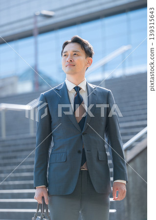 A business image of success and growth, featuring a sharp-looking salesman in a suit, gazing into the future against the backdrop of an office building and staircase. A business image of success and growth, featuring a sharp-looking salesman in a suit, gazing into the future against the backdrop of an office building and staircase. 139315643