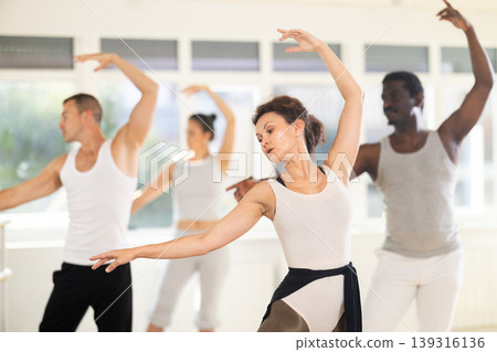 Female ballet dancer performing dance moves at group rehearsal Female ballet dancer performing dance moves at group rehearsal 139316136
