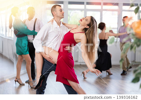Elegant duet of a man and a woman in festive dresses dances a passionate tango during a group dance lesson in choreographic studio 139316162