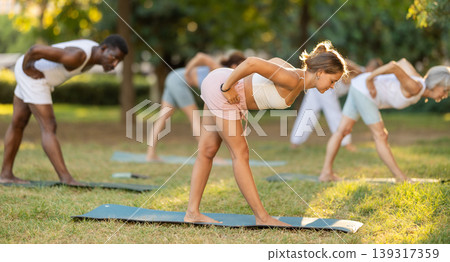 Girl performing Pyramid Pose during group young class in park Girl performing Pyramid Pose during group young class in park 139317359