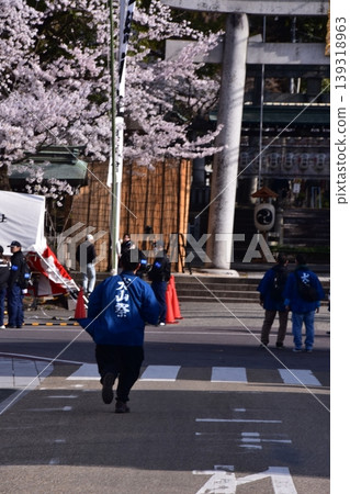 A man participating in the Inuyama Festival in Inuyama City, Aichi Prefecture, walking while wearing a happi coat with "Inuyama Festival" written on it, with cherry blossoms in full bloom and the torii gate of Haritsuna Shrine in the background. A man participating in the Inuyama Festival in Inuyama City, Aichi Prefecture, walking while wearing a happi coat with "Inuyama Festival" written on it, with cherry blossoms in full bloom and the torii gate of Haritsuna Shrine in the background. 139318963