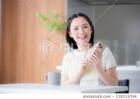 A smiling woman in an apron, like a housewife, tapping on her smartphone. 139319394