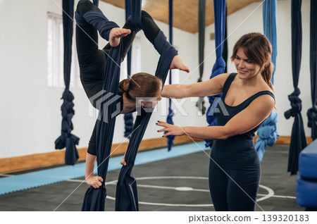 Process of doing spine exercise. Female instructor helping a child practice aerial yoga on hammock straps in a fitness studio 139320183