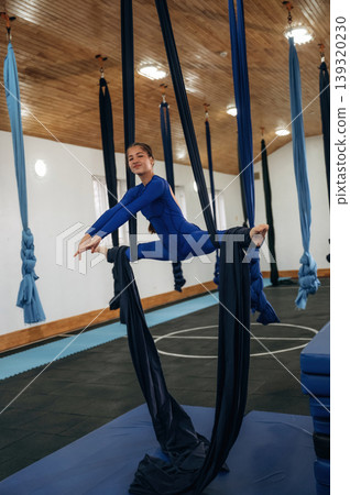 In blue sportive clothes. Child practicing aerial yoga on hammock straps in a fitness studio 139320230