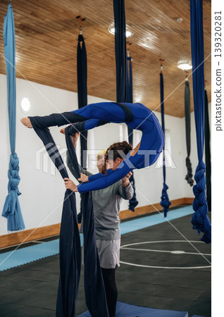 Black color hammock straps. Male instructor assisting a child in aerial yoga practice in a fitness studio Black color hammock straps. Male instructor assisting a child in aerial yoga practice in a fitness studio 139320281