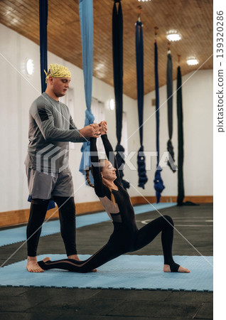 Man is teaching. Male instructor assisting a child during yoga practice in a fitness studio 139320286