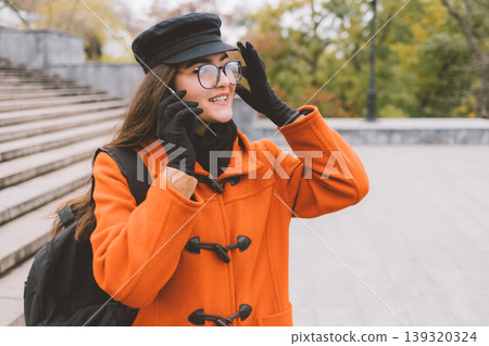Smiling woman in orange coat talks on phone outdoors 139320324