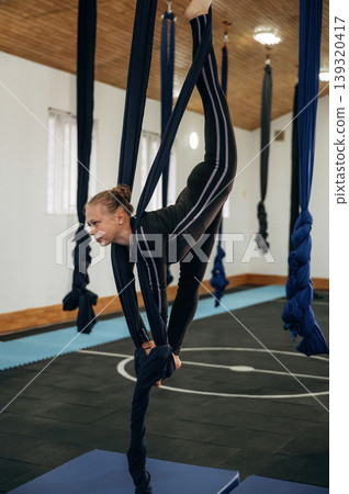 Balancing, doing tricks. Child practicing aerial yoga on hammock straps in a fitness studio 139320417