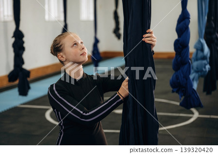 Black clothes, flexibility conception. Child practicing aerial yoga on hammock straps in a fitness studio Black clothes, flexibility conception. Child practicing aerial yoga on hammock straps in a fitness studio 139320420