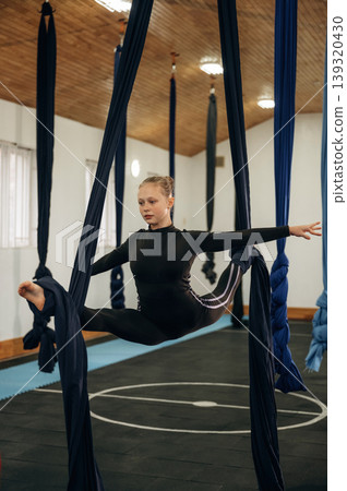 Up in the air. Child practicing aerial yoga on hammock straps in a fitness studio 139320430