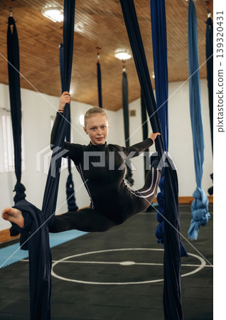 Up in the air. Child practicing aerial yoga on hammock straps in a fitness studio Up in the air. Child practicing aerial yoga on hammock straps in a fitness studio 139320431