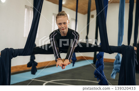 Up in the air. Child practicing aerial yoga on hammock straps in a fitness studio Up in the air. Child practicing aerial yoga on hammock straps in a fitness studio 139320433