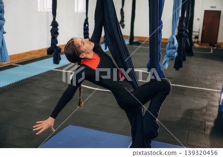 Hobby conception, up in the air. Child practicing aerial yoga on hammock straps in a fitness studio Hobby conception, up in the air. Child practicing aerial yoga on hammock straps in a fitness studio 139320456