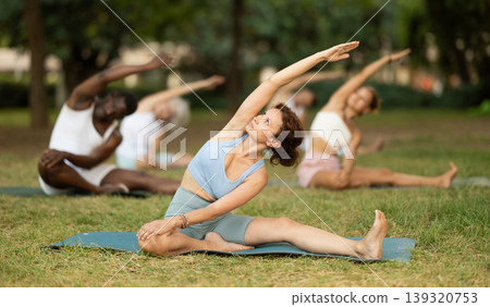 Woman performing Parivrtta Janu Sirsasana during group yoga class in park Woman performing Parivrtta Janu Sirsasana during group yoga class in park 139320753