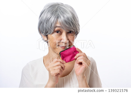 A senior woman happily holds a pink coin purse in both hands. A senior woman happily holds a pink coin purse in both hands. 139321576