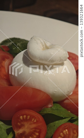 Fresh burrata cheese served on a plate with sliced tomatoes and basil leaves, showcasing creamy texture and vibrant colors in a culinary presentation Fresh burrata cheese served on a plate with sliced tomatoes and basil leaves, showcasing creamy texture and vibrant colors in a culinary presentation 139321664