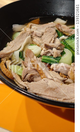 Asian-style soup featuring tender sliced pork, bok choy, and assorted vegetables in a black pot, placed on a vibrant orange surface Asian-style soup featuring tender sliced pork, bok choy, and assorted vegetables in a black pot, placed on a vibrant orange surface 139321681