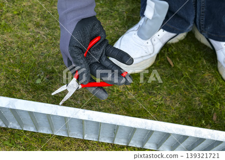 A person wearing gloves holds a pliers during a drain grate maintenance, focusing on proper safety gear and careful handling 139321721