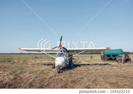 man in protective mask refueling small white aircraft on grassy airfield, aviation worker in uniform, sunset, rural field, aviation service, pilot training, countryside tourism 139322215