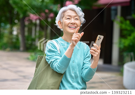 一位老年婦女面帶微笑，手持智慧型手機擺姿勢拍照。 139323211