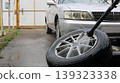 Washing car tires with a hose and a watering can in the yard of a house against the background of a gray car, tire care when changing a tire 139323338