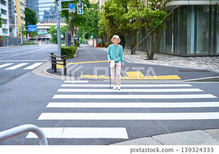 A senior woman with a cane stands in front of a crosswalk. A senior woman with a cane stands in front of a crosswalk. 139324333