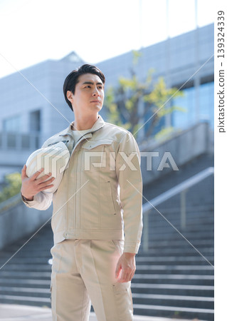 一幅年輕工人手持安全帽，仰望建築工地和建築物的肖像，象徵成長、未來和希望。 139324339