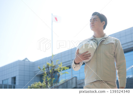 一幅年輕工人手持安全帽，仰望建築工地和建築物的肖像，象徵成長、未來和希望。 139324340