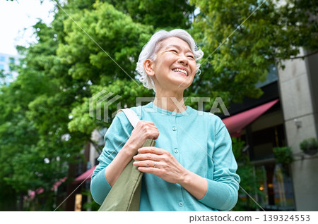 一位老婦人抬起頭,雙手拿著環保袋。 一位老婦人抬起頭,雙手拿著環保袋。 139324553