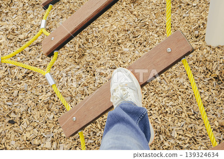 Person balancing on wooden plank bridge in a playground. Joy of simple challenges. Person balancing on wooden plank bridge in a playground. Joy of simple challenges. 139324634
